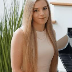 W&J alumna Caroline Fedor '20 sit on a piano bench and smiles.