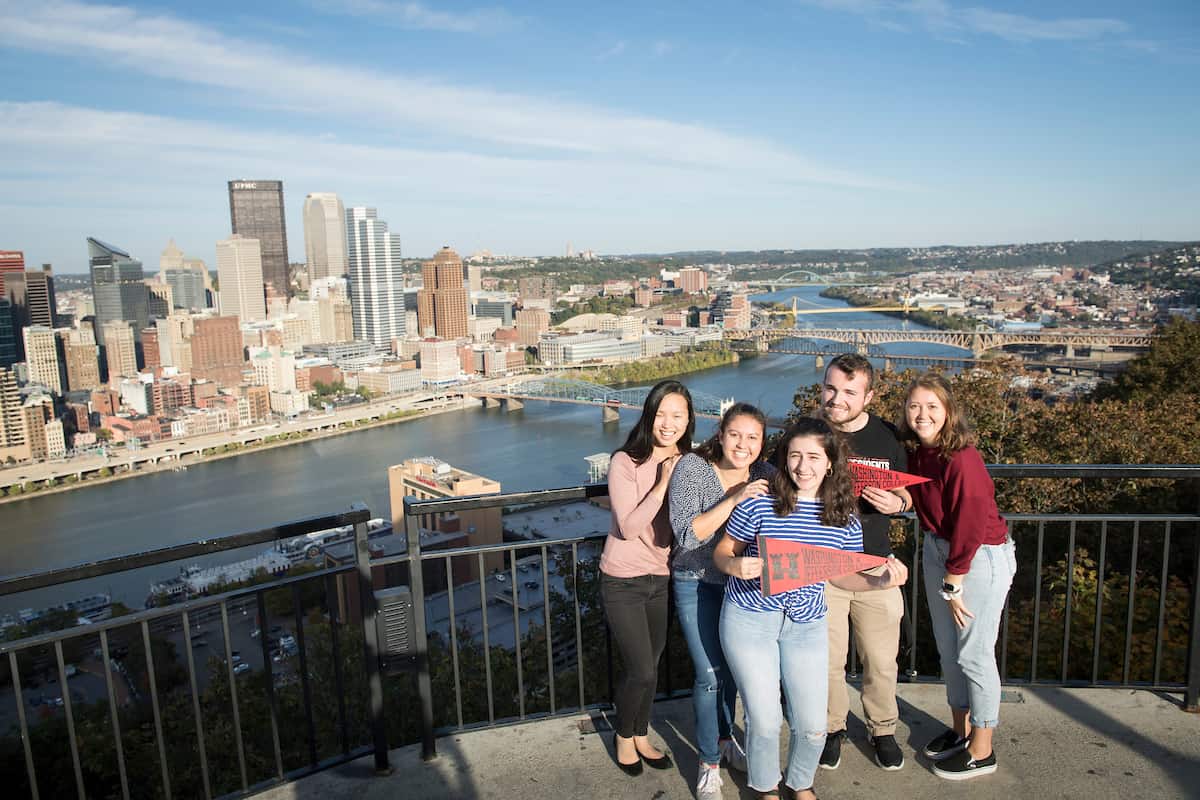 Students pose with a pennant as they look out over the city of Pittsburgh from Mount Washington October 21, 2019 during the Creosote Affects photo shoot at Washington &amp; Jefferson College.