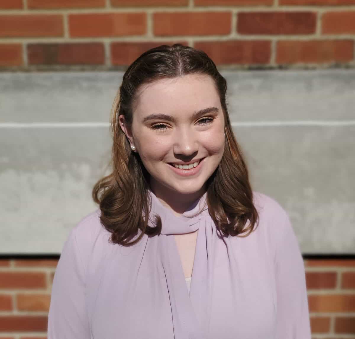 W&J senior English major Hannah Lindsay smiles in front of a brick wall.